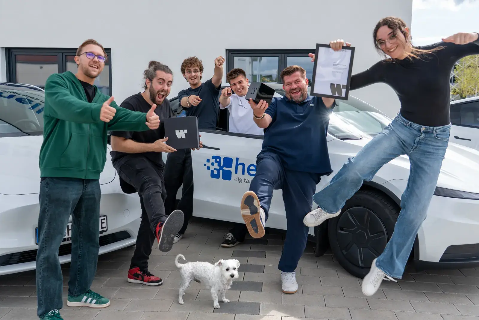 Das Team von Heller Digitales Marketing jubelt mit der Urkunde vor dem Firmenwagen