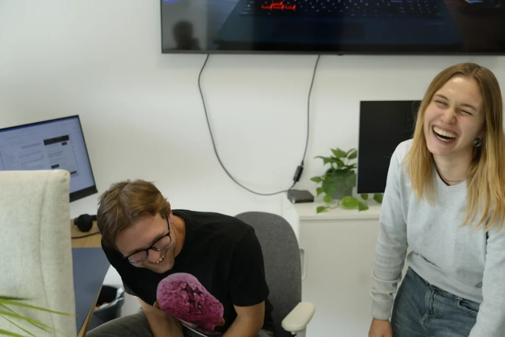 Milena Birkel lacht mit einem Kollegen im Besprechungsraum