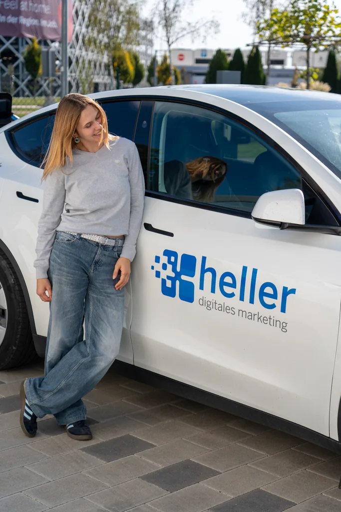 Milena Birkel lehnt am Firmenwagen von Heller Digitales Marketing
